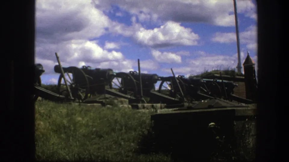 1975 Copenhagen 8mm frame of preserved wheeled cannons in a grassy outdoor display, with heavy clouds overhead.