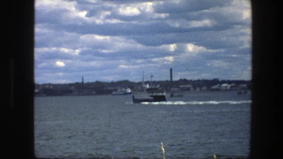 Copenhagen harbor scene from 1975 with the ferry near center, small boats nearby, and industrial waterfront details in the distance.