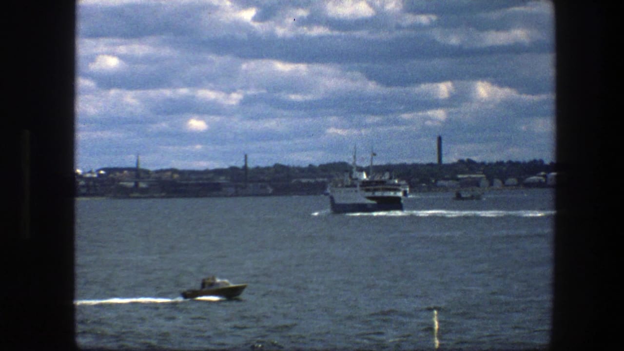 Small motorboat passes in front of a distant ferry on choppy harbor water.