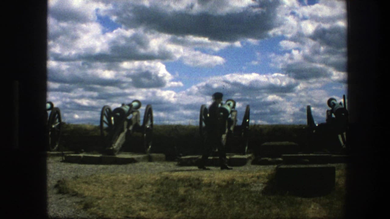 In 1975 Copenhagen, a lone man appears in silhouette while walking past historic cannons on a grassy site under a cloudy sky.