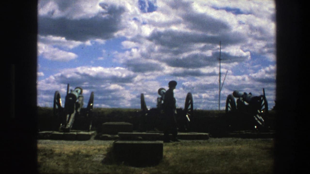 1975 8mm Copenhagen frame with a dark figure walking past historic cannons on grass, seen through heavy shadowed framing.