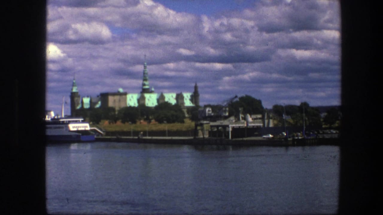 Blue-and-white boat on calm water with green-roofed historic buildings in the distance.