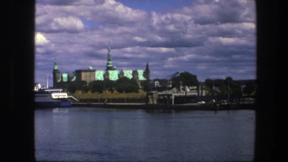 1975 Copenhagen 8mm view of a blue-and-white boat on calm water with green-roofed historic buildings beyond.