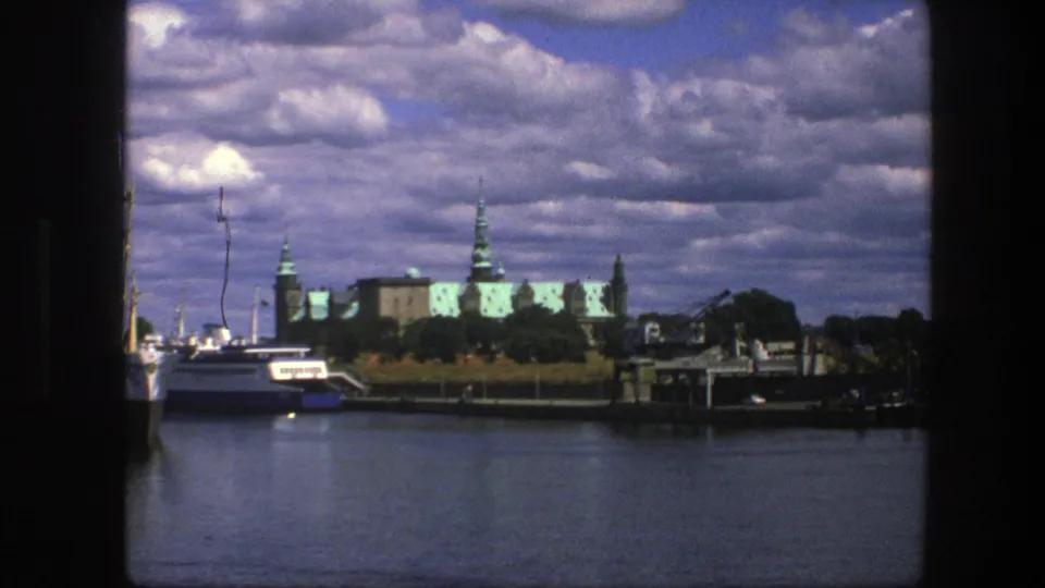 1975 Copenhagen travel frame showing a boat on calm water with green-roofed historic buildings and docks behind it.