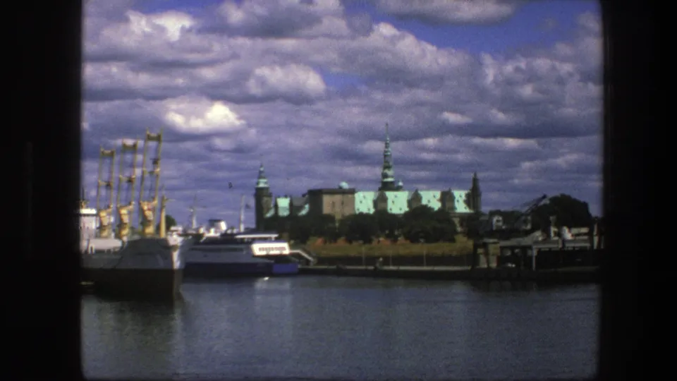 1975 Copenhagen harbor frame with boats and masts in front of green-roofed palace architecture and broad clouds.