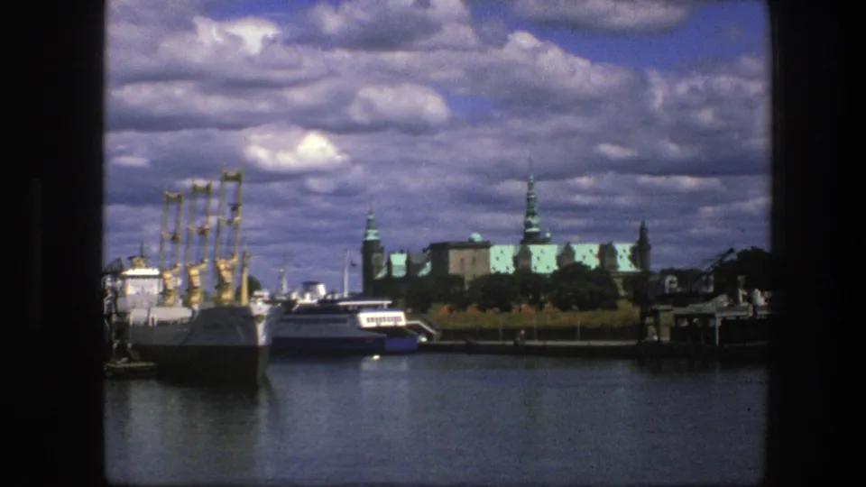 Copenhagen harbor view from 1975 with white boats, calm water, palace architecture, trees, and a sky of puffy clouds.