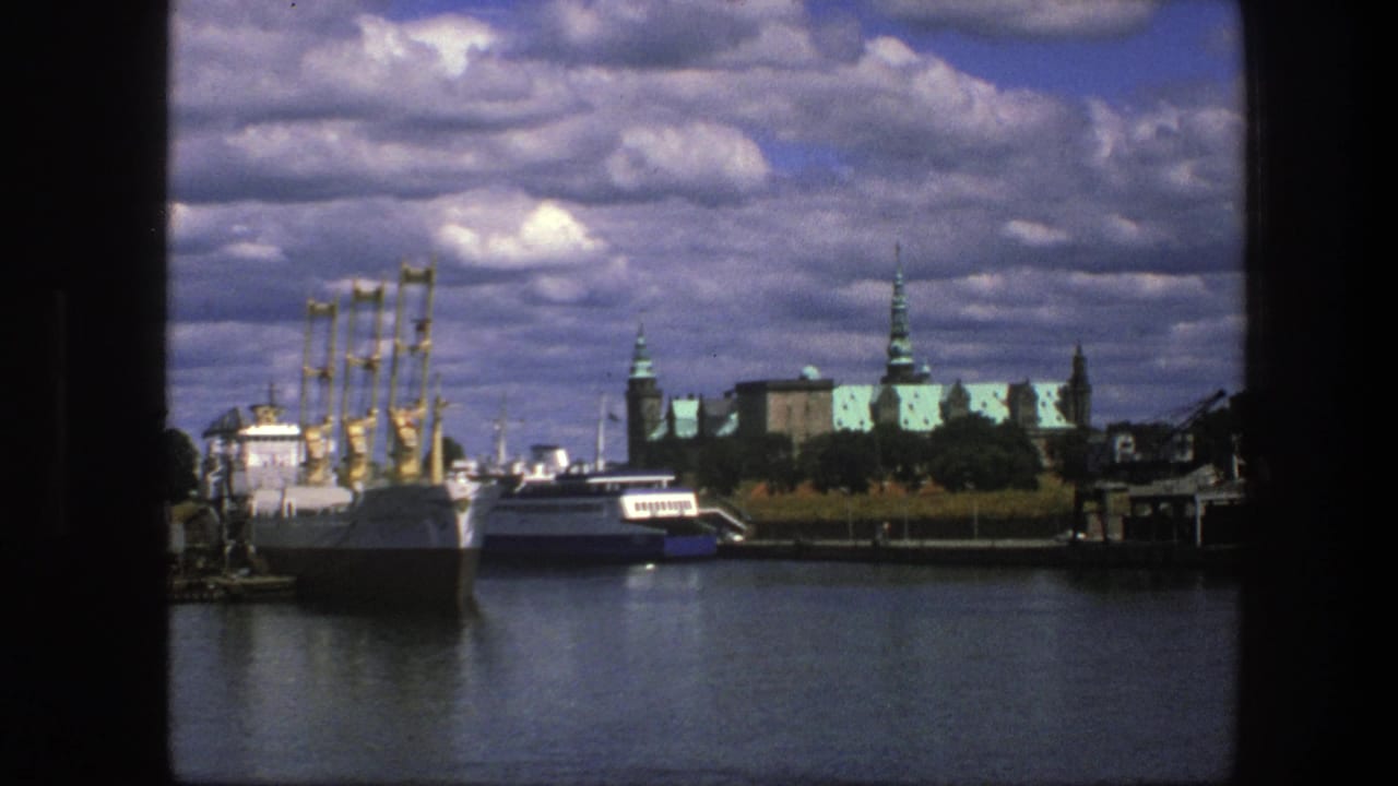 Docked boats and yellow cranes across calm water under a cloudy sky.