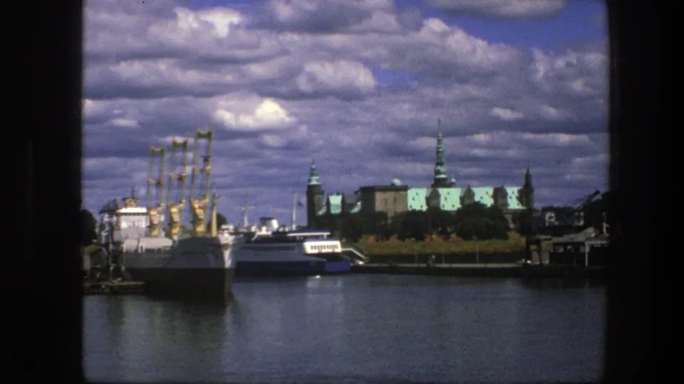 1975 Copenhagen harbor view with docked vessels, yellow cranes, historic rooftops, and calm water seen through dark frame edges.