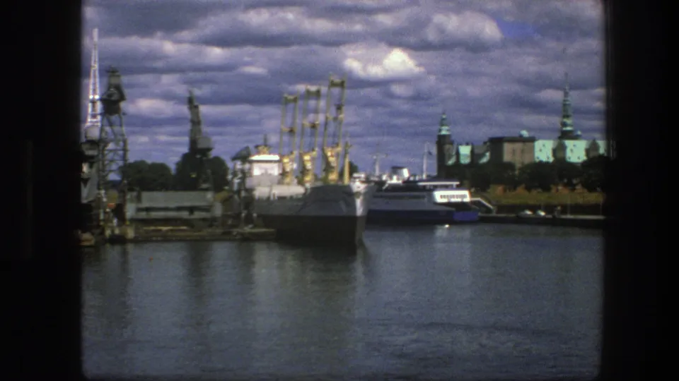 Copenhagen harbor footage from 1975 with docked vessels, yellow cranes, green-roofed architecture, and layered clouds over reflective water.