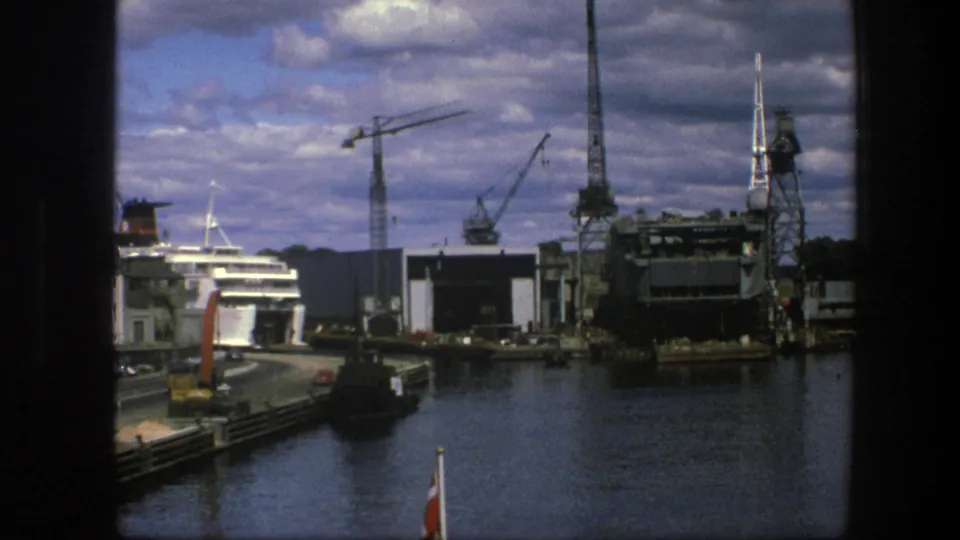 Copenhagen harbor in 1975 with cranes and dock buildings around a moored passenger ship, framed by dark vertical edges.