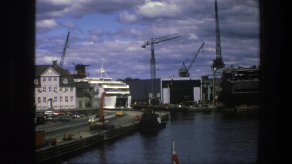 Copenhagen harbor footage from 1975 showing a passenger ship at the pier, cranes, road traffic, water, and a cloudy sky.