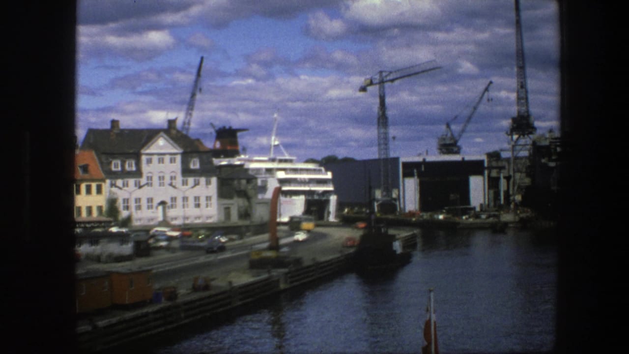 Harbor road, white ship, dock cranes, buildings, water, and dark frame edges.