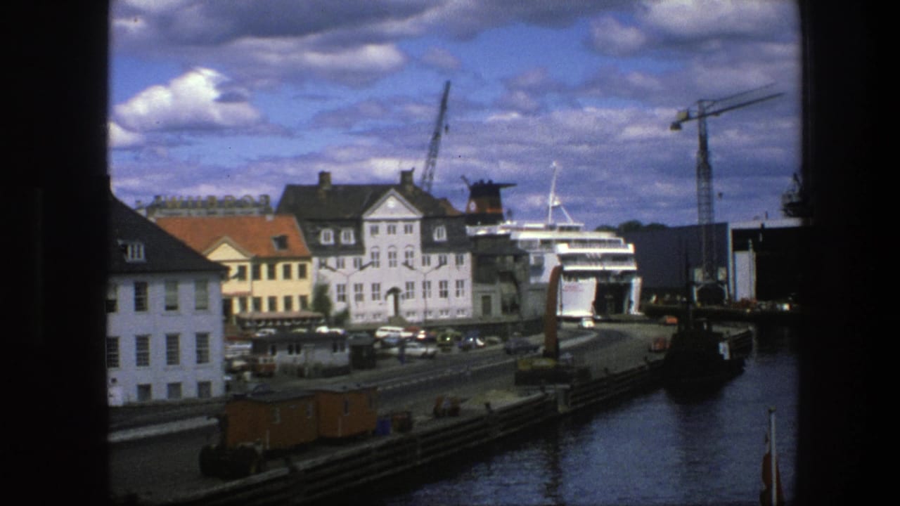 Waterfront buildings, docked ship, cranes, road traffic, and blue sky seen through dark frame edges.
