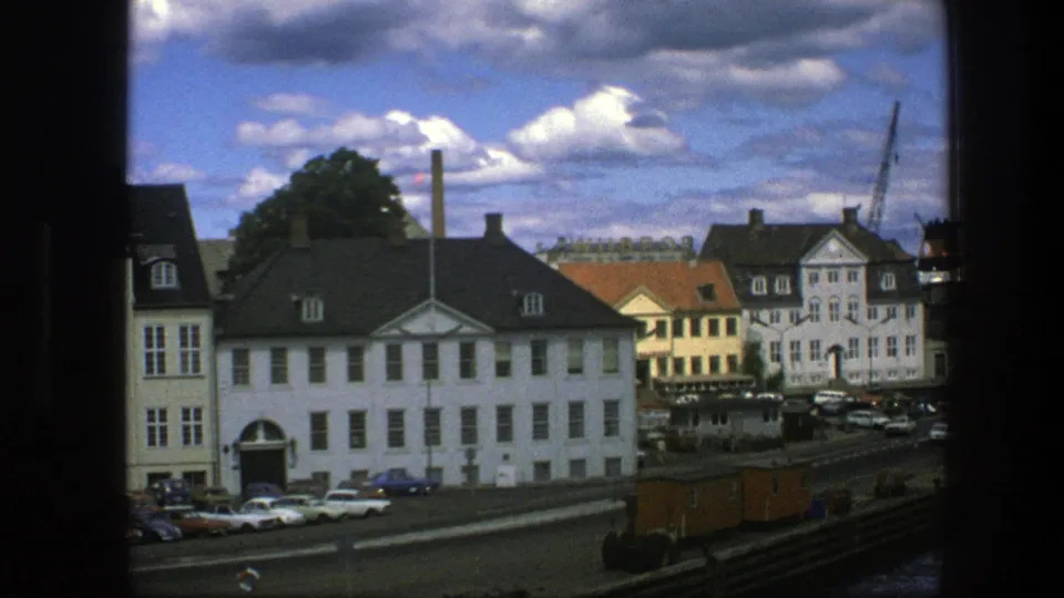 Copenhagen harbor footage from 1975 showing a white waterfront building, parked cars, harbor edge, cranes, a docked ship, and bright clouds.