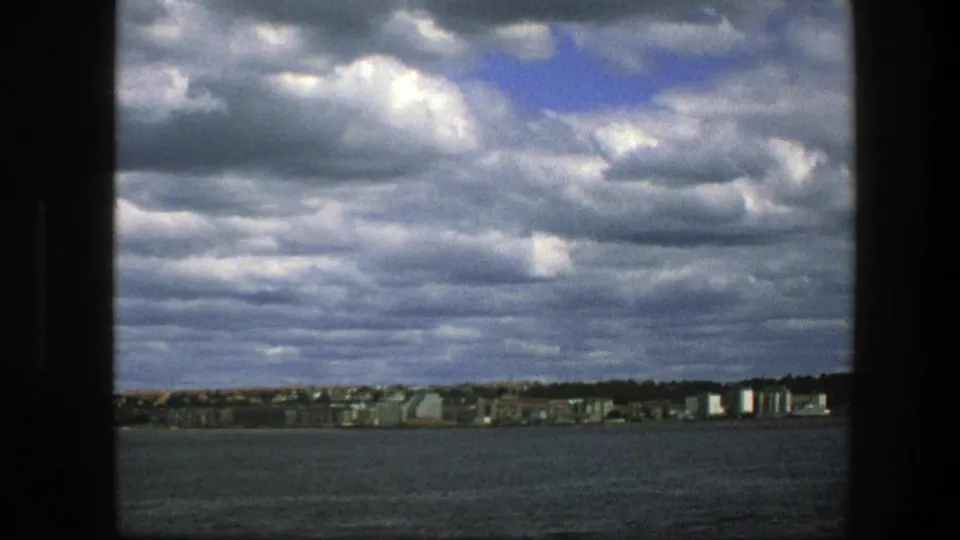 Copenhagen shoreline at the end of the pan, with water in the foreground and dense clouds above distant buildings.