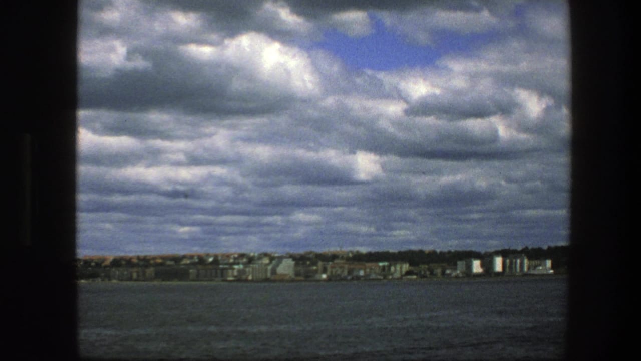 Distant waterfront across open water under a cloudy sky, framed by dark boat edges.