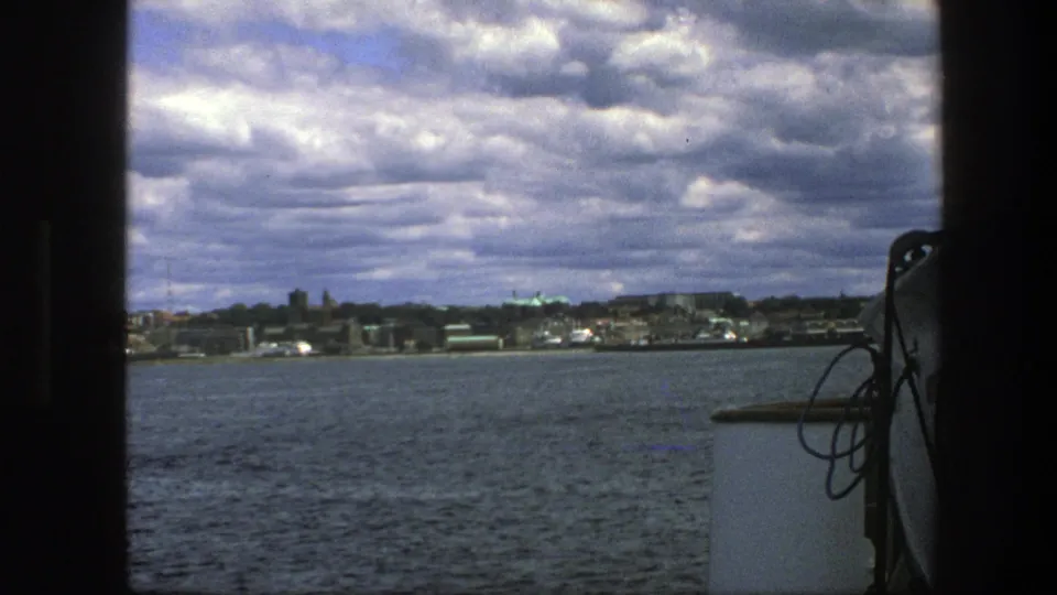 1975 8mm view from a boat toward a distant Copenhagen waterfront beneath a cloudy sky.