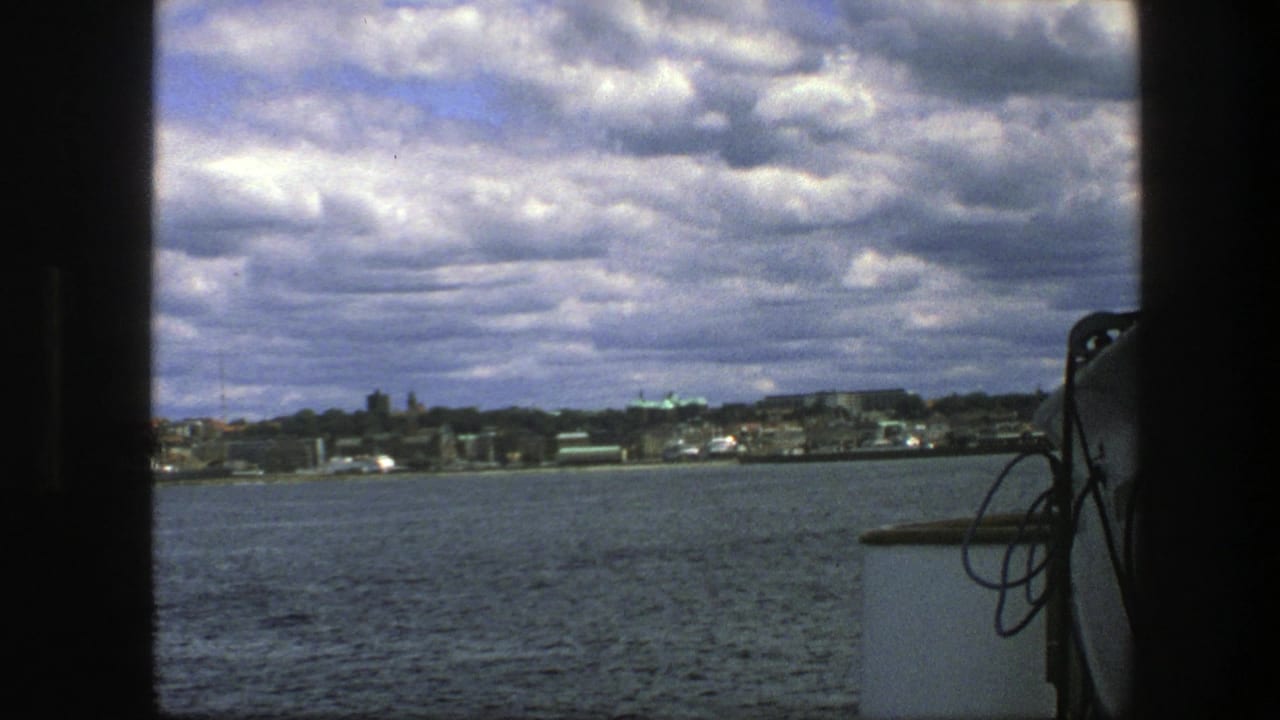 Copenhagen waterfront and cloudy sky filmed from the water, with the boat edge in the foreground.