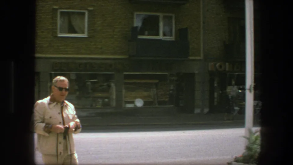 The Copenhagen street scene shows the man partly at frame edge, still holding his camera before brick buildings and shopfronts.