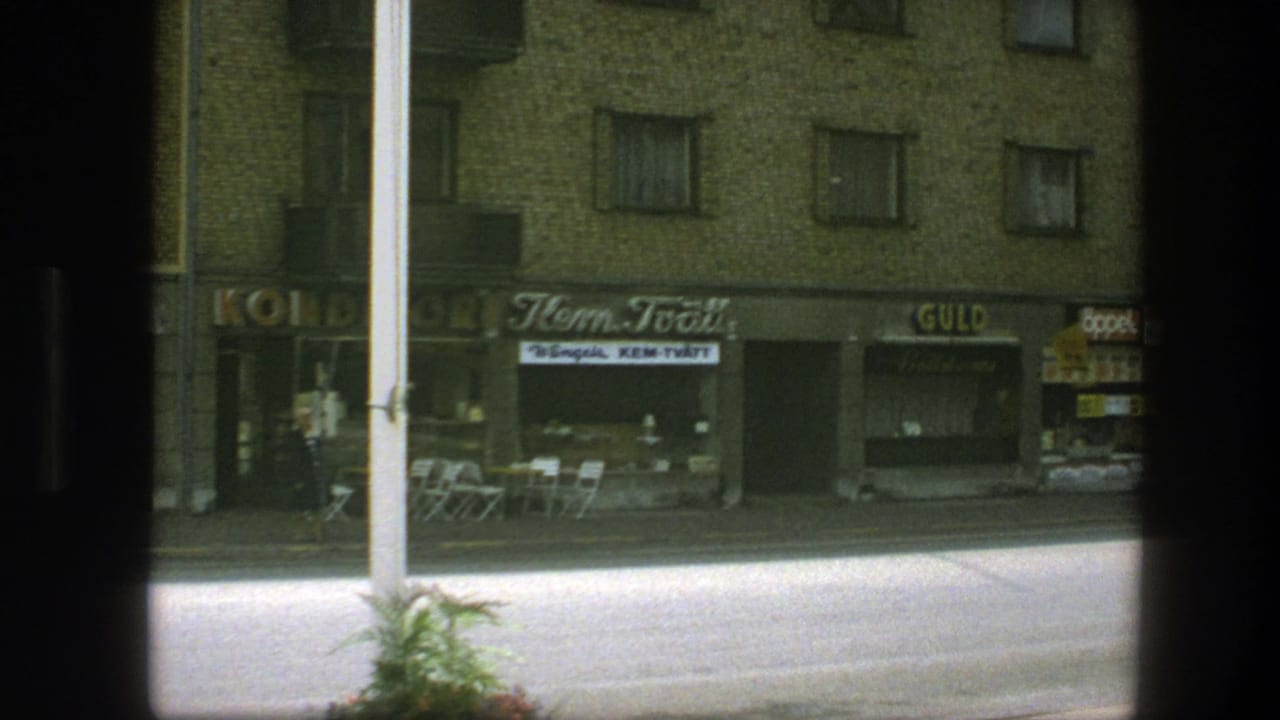 Copenhagen street view from 1975 showing small shops, brick upper floors, outdoor seating, and a car partly visible in shadow.