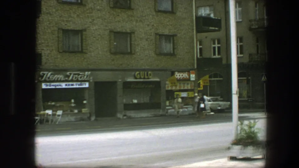 Copenhagen 1975 street scene with small shopfronts, pedestrians near a corner, and a yellow car passing or parked at the curb.