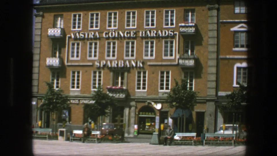 Copenhagen 1975 home-movie view of the Vastra Goinge Harads Sparbank facade, with plaza benches, small trees, and people near the entrance.