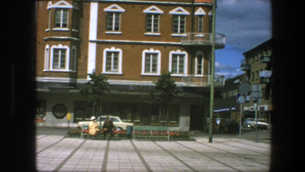 Brick corner building facing a tiled plaza with pedestrians and street signs.