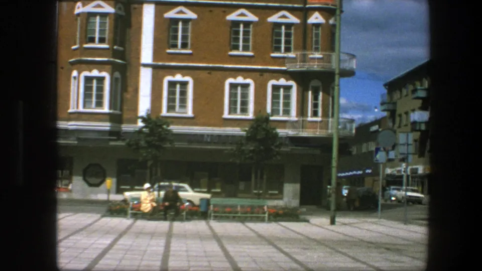 Copenhagen street view from 1975 showing a brick corner building, tiled paving, pedestrians, signs, and parked cars.