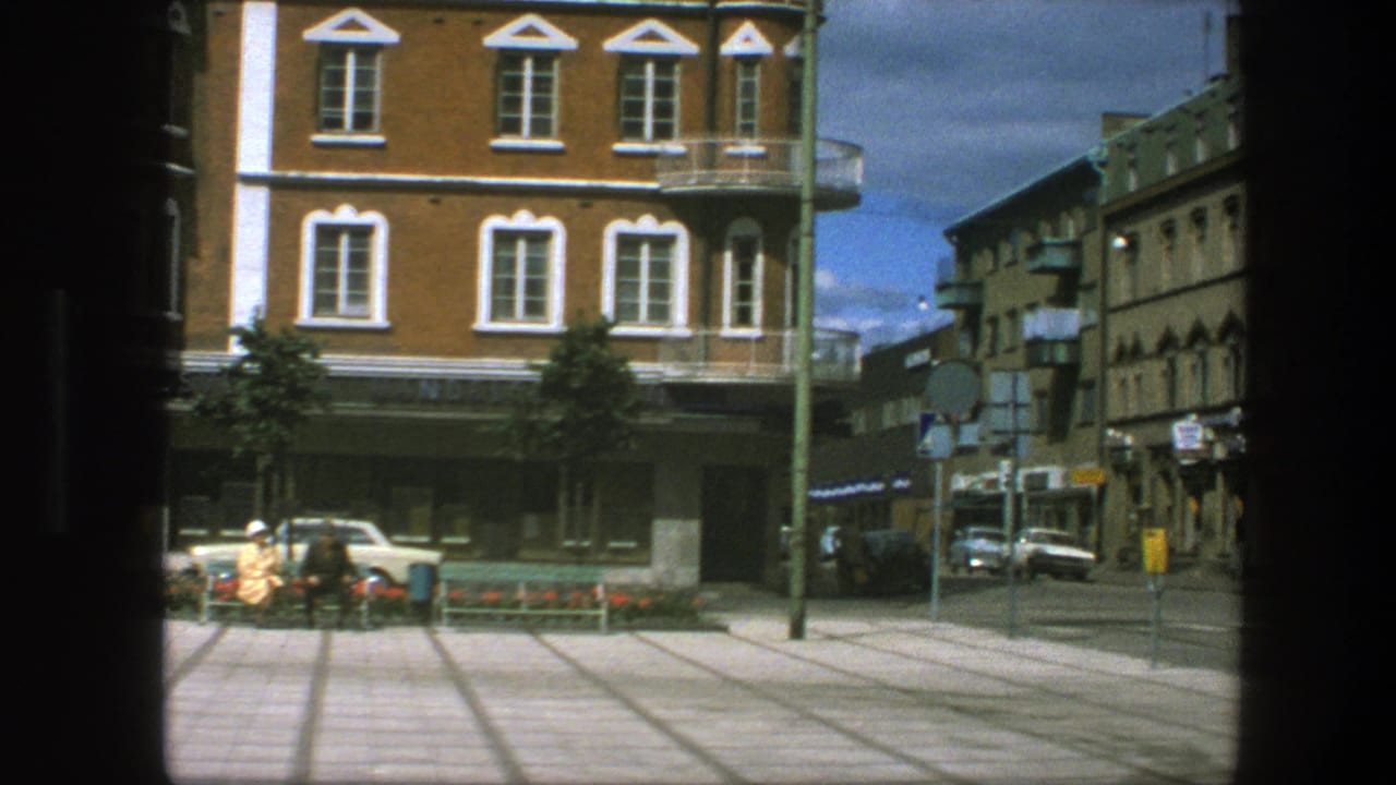 Street corner with brick building, tiled paving, pedestrians, signs, and cars.