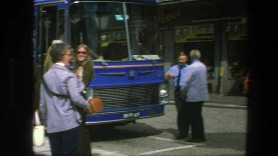 Copenhagen 1975 street scene with a blue bus, pedestrians near the curb, and storefronts behind the bus stop.