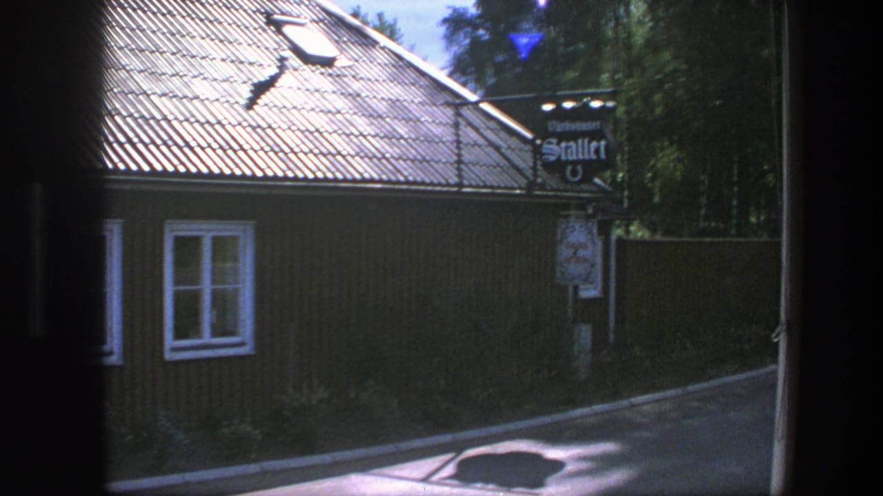 Dark wooden building with white windows, tiled roof and a hanging sign near the road.