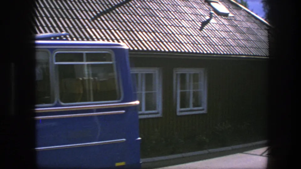 The passing blue van fills much of the foreground while the 1975 Copenhagen wooden building remains visible behind it.