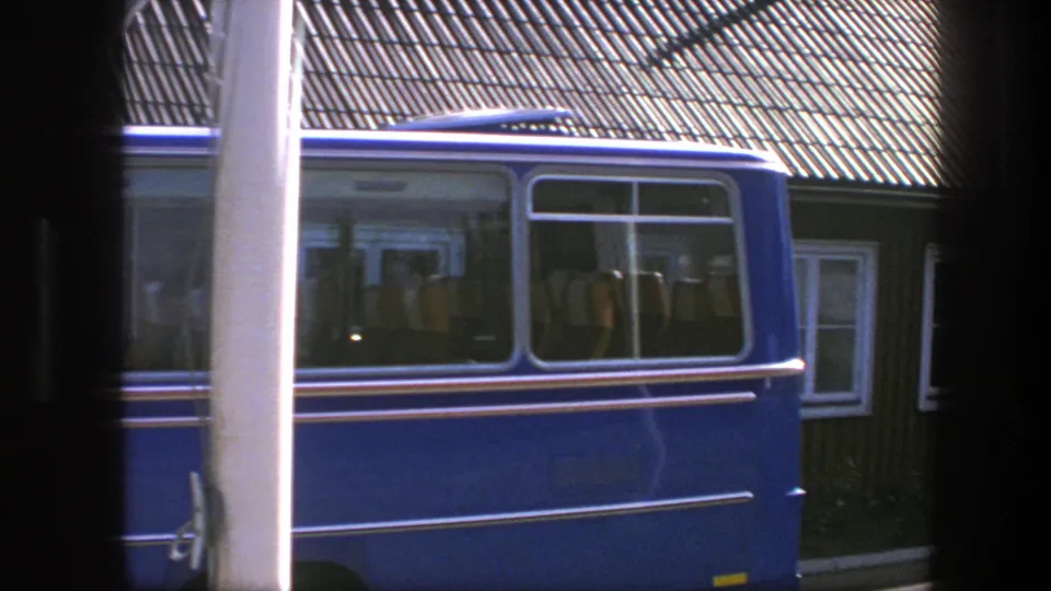A white pole and blue van partially block the 1975 Copenhagen building, with roof, windows and facade still visible behind them.
