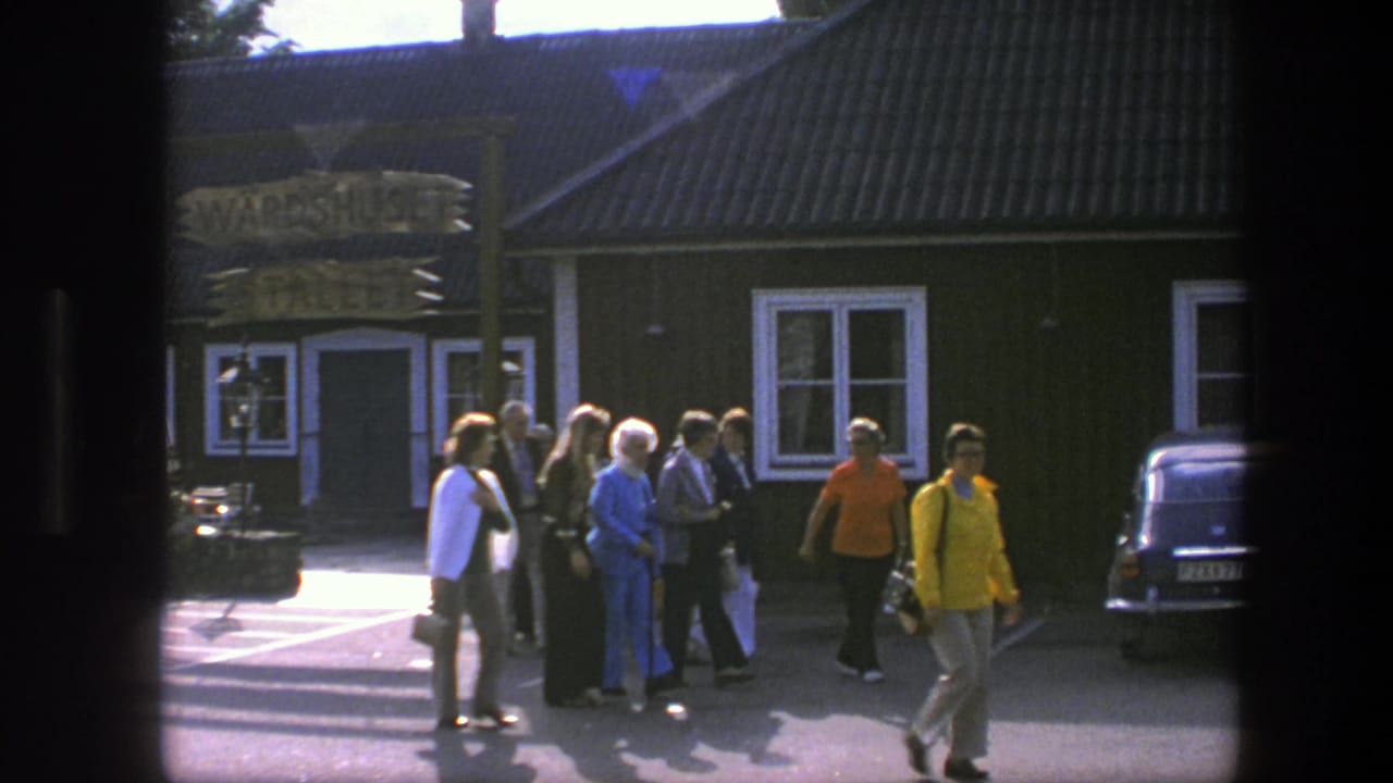 A small group in 1970s clothing crosses the paved foreground outside the green Copenhagen building as a dark car sits at right.