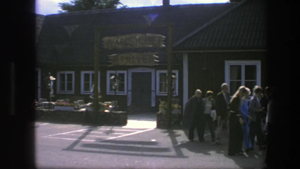 Near the end of the clip, the pedestrians move out of view beside the 1975 Copenhagen building while the sign and facade remain central.