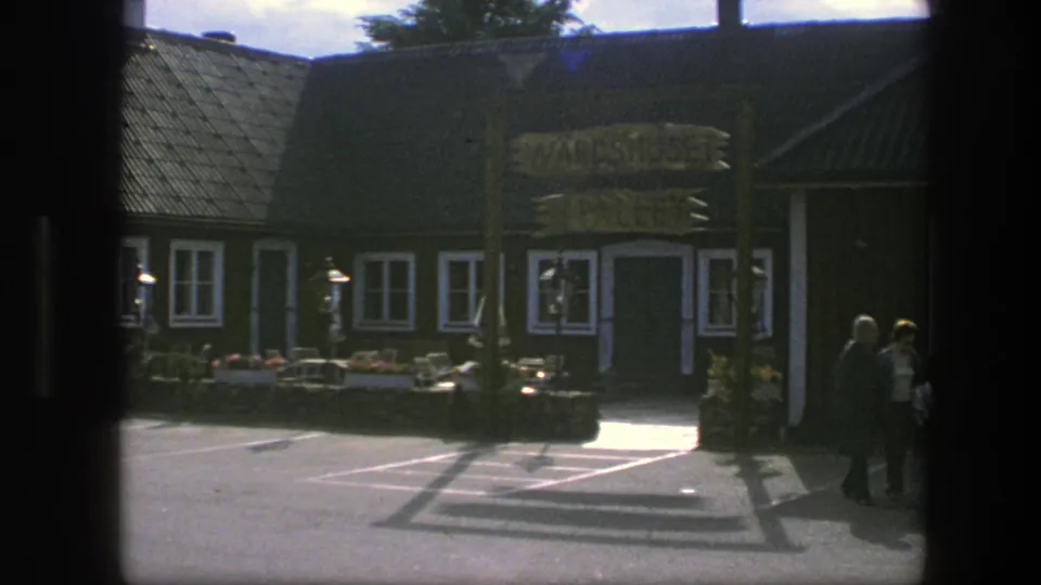 1975 Copenhagen street view showing a brown-and-white building facade, entrance sign, flower boxes, and people walking near the door.