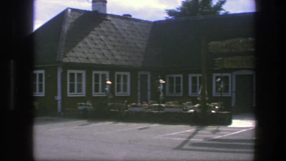 1975 Copenhagen exterior with a traditional brown building, white window trim, tiled roof, wooden signage, and flower boxes along the front.