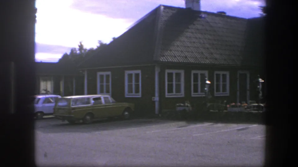 1975 Copenhagen street scene with parked period cars beside a brown-and-white building under bright daylight.