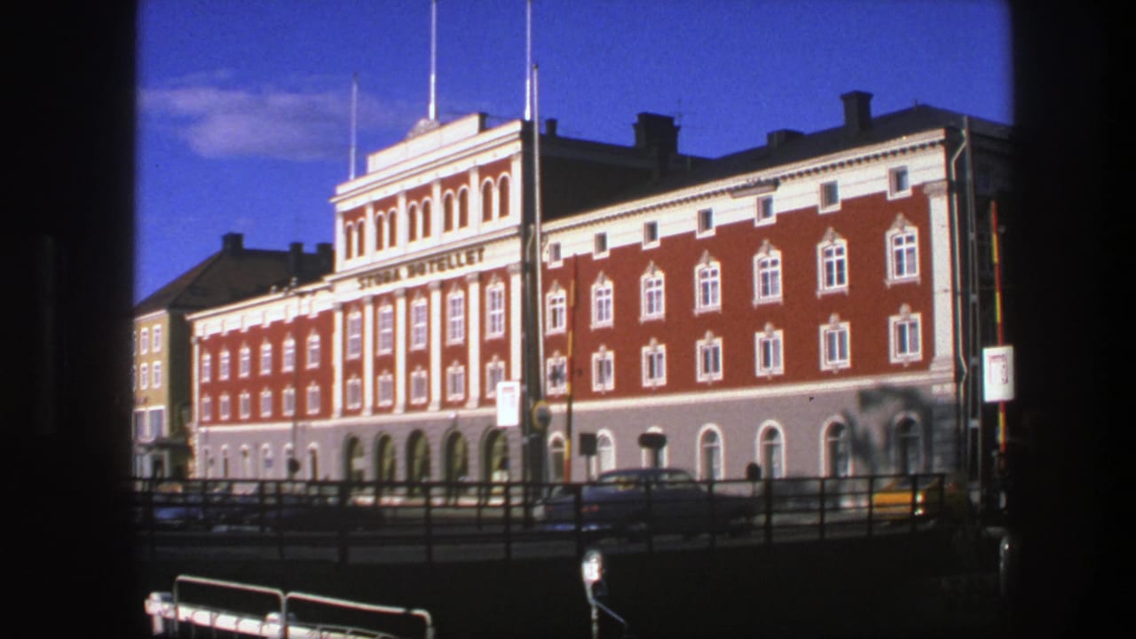 Red brick hotel facade with white trim, street railings, cars, and blue sky.
