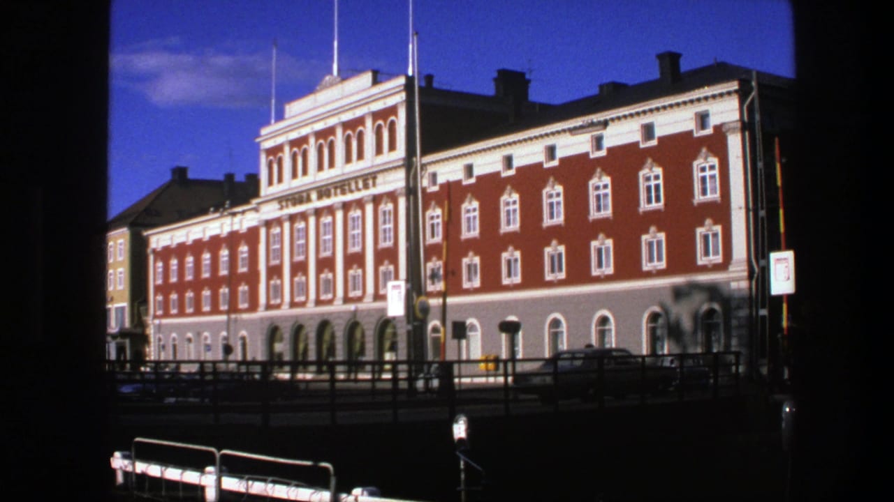 1975 Copenhagen home-movie frame showing a red and white hotel facade across a bridge or waterfront railing.