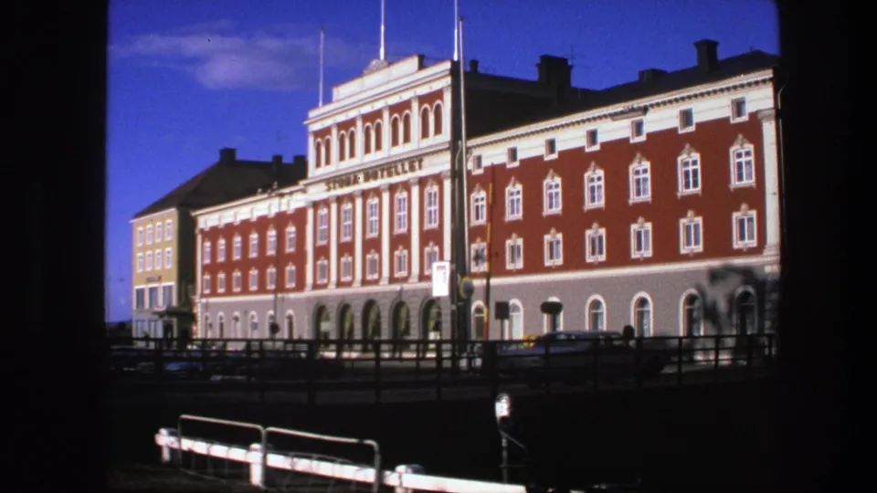 1975 Copenhagen frame showing the hotel facade beside a yellow building, with railings and cars in front.