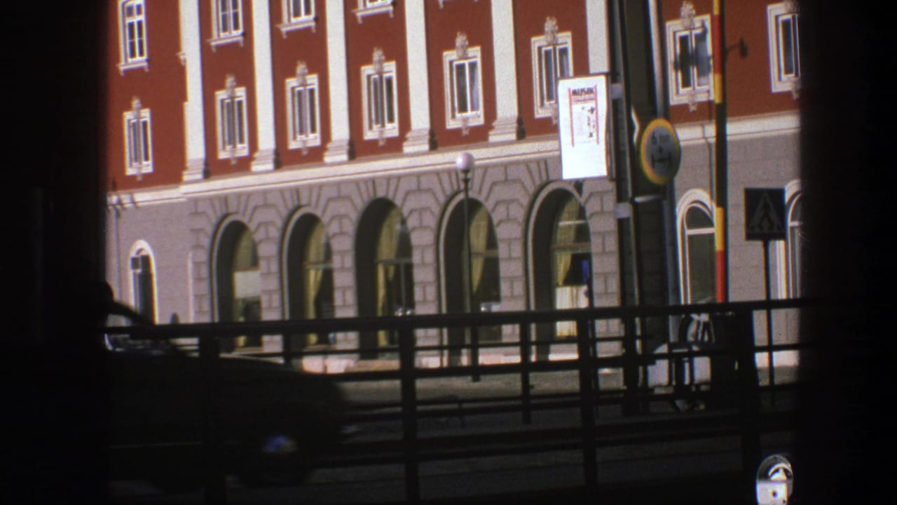 Ornate red building facade with arched windows, street railing, signs, and a dark car blur.