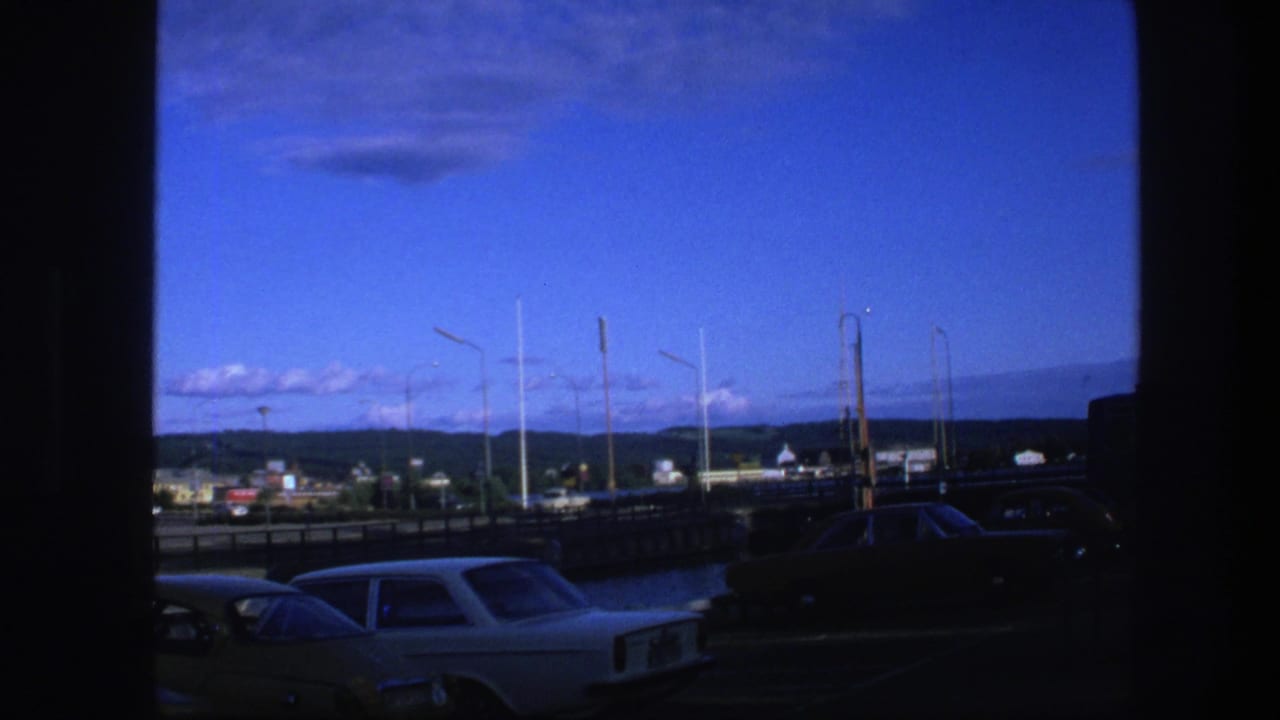 View across a road with classic cars, streetlights, low buildings, distant hills, and blue sky.