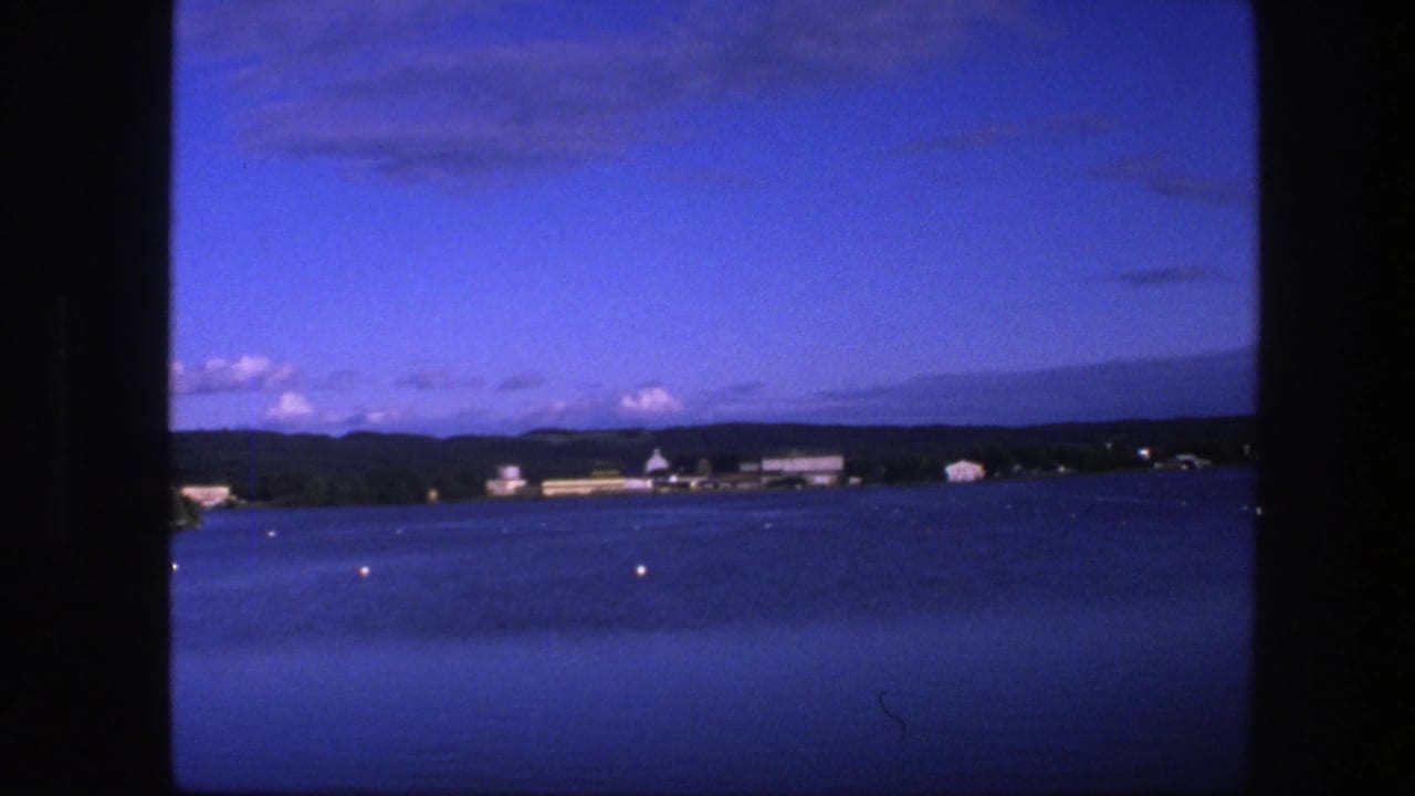 Calm water with small buoys and a distant Copenhagen shoreline under a blue sky.