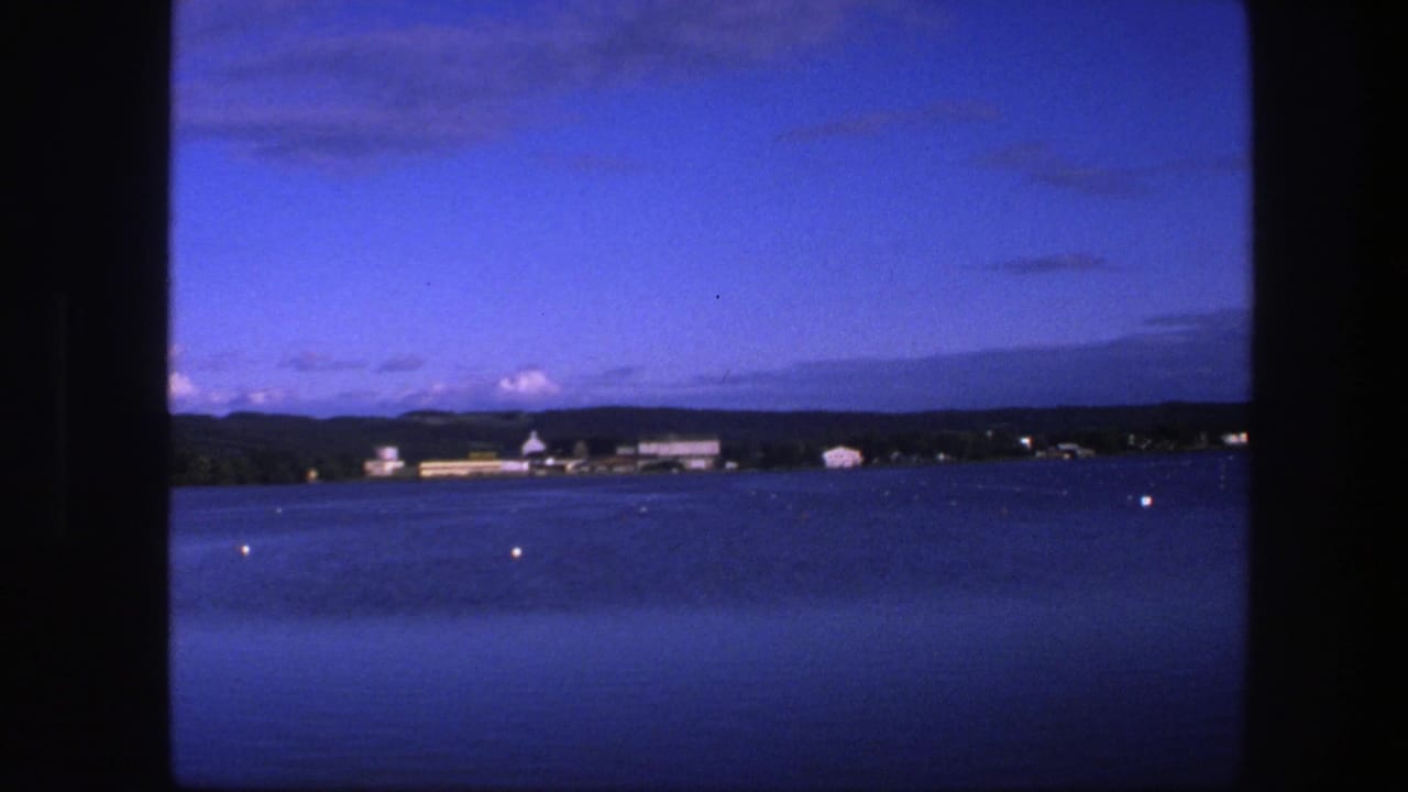 Distant shoreline buildings beyond blue water, with small buoys in the foreground.