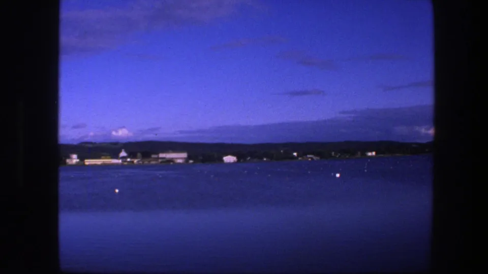 Copenhagen waterfront seen from the sea on 8mm film in 1975, with calm water, buoys, low buildings, clouds, and dark frame borders.