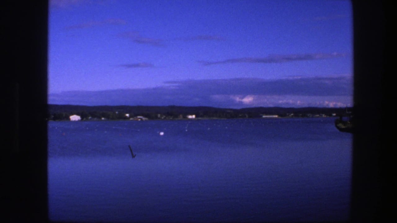 Calm blue water and a distant shore viewed through a window at dusk.