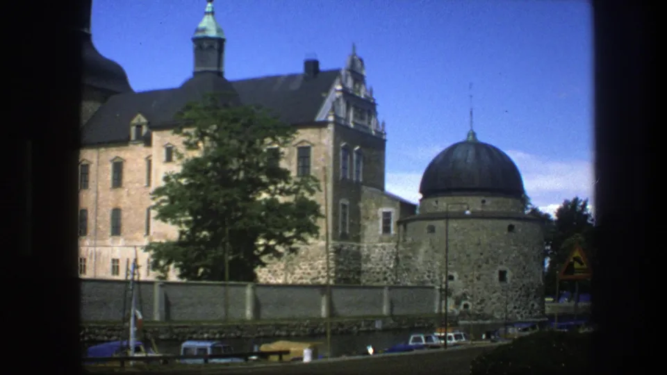 A handheld Copenhagen 1975 travel frame shows older stone architecture, a domed structure, trees, walling, cars, and a road sign.