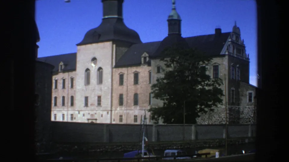 1975 Copenhagen frame showing the castle-like exterior through dark side framing, with domed tower, spire, tree, wall, and cars below.
