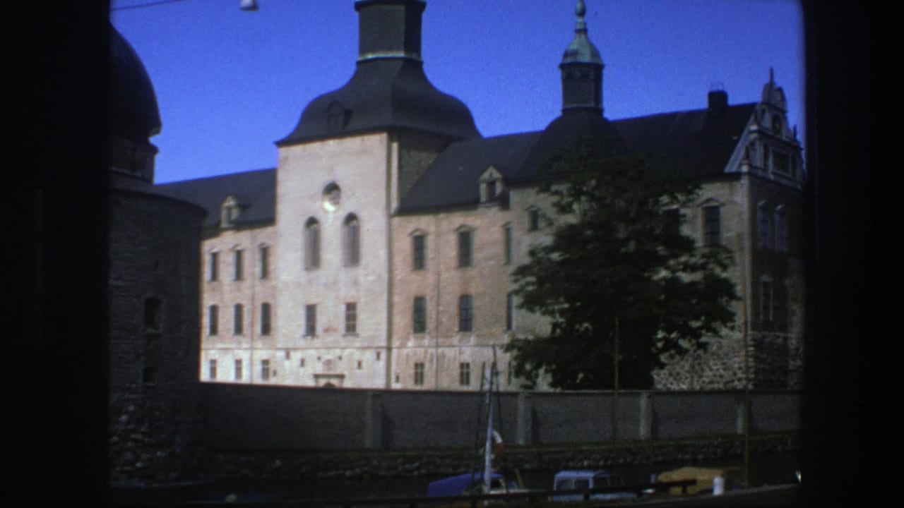 Historic stone building with towers seen across water, partly framed by dark foreground edges.